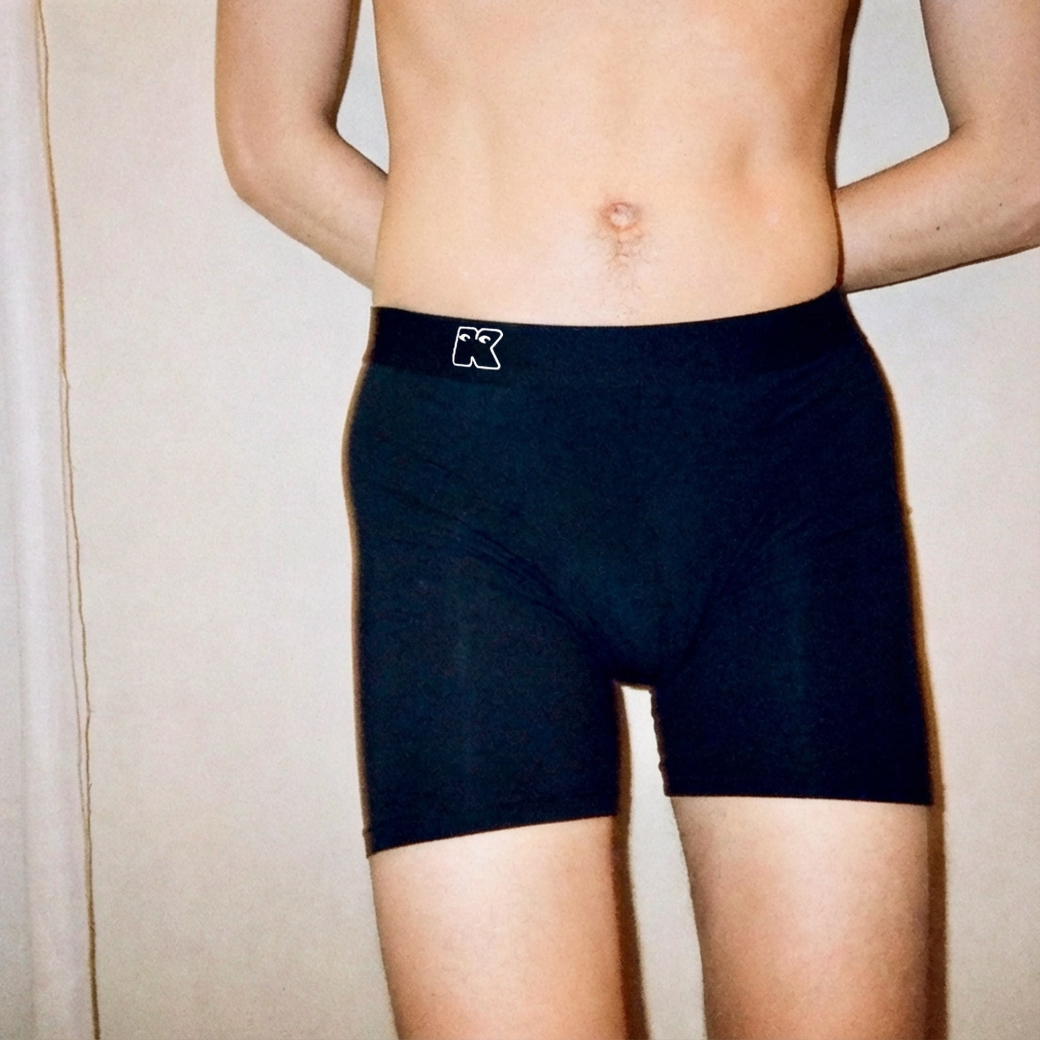Person wearing black boxer briefs with a brand logo on a neutral background