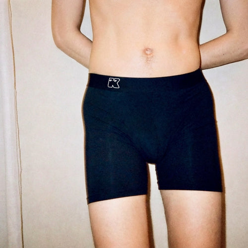 Person wearing black boxer briefs with a brand logo on a neutral background